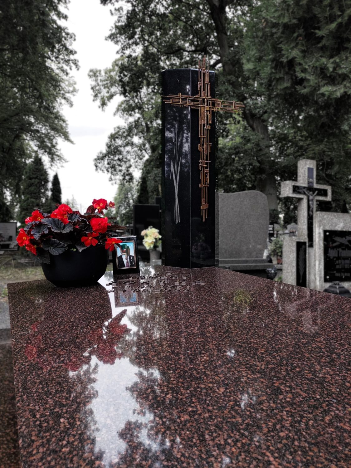 Nagrobek granitowy czerwony z czarnym słupem i miedzianym krzyżem